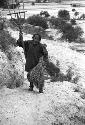 Old woman on path holding bundle of hay and pitchfork