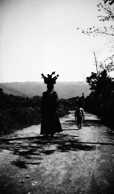 Woman and child with baskets filled with goods on their heads walking on road