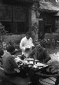 Eleanor Lattimore, a man and a woman seated at table in courtyard