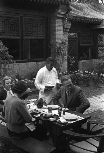 Eleanor Lattimore, a man and a woman seated at table in courtyard