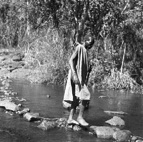 Masai native crossing stream on stepping stones