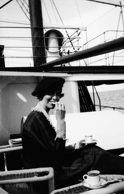 Woman holding cup and sitting on deck of ship