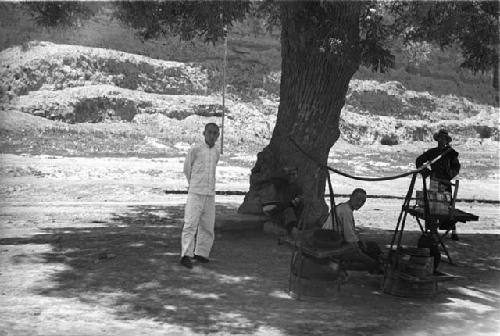 Four men under a tree with table and apparatus