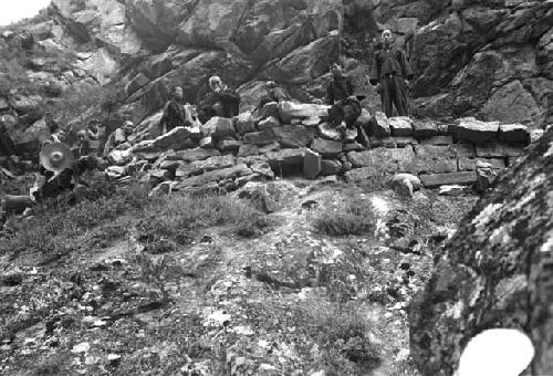 Several people sitting and standing on wall, on side of mountain