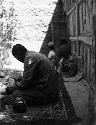 Sanju bazaar, sideview of Moses cooking and sitting in front of wooden building