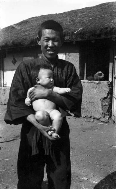 Solun Mongol and baby, standing in front of a building