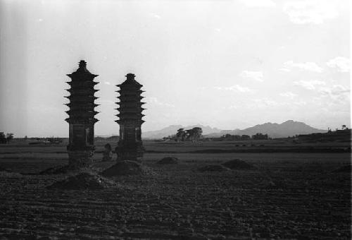 Two tall, narrow pagodas and several mounds in a field