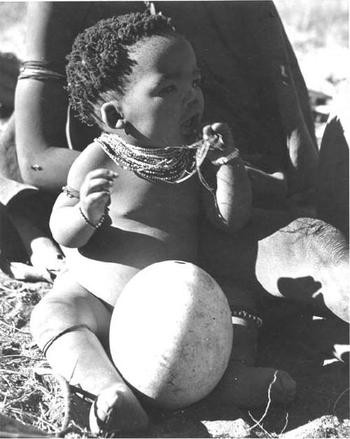 Baby (child of ≠Gao, leader of Band 10, and Bau, his first wife) sitting next to an ostrich eggshell