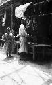 Old butcher and boy in front of a stall, meat and scales hanging in background