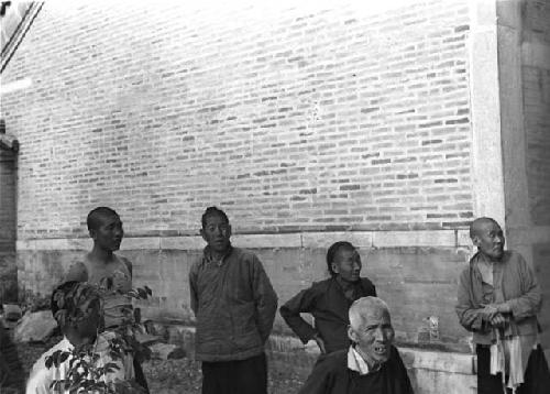 Group of seven people standing by brick building wall