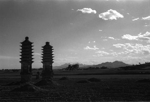 Two tall, narrow pagodas and several mounds in a field