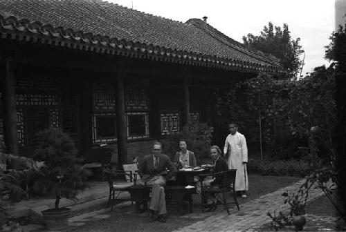 Eleanor Lattimore, a man and a woman seated at table in courtyard