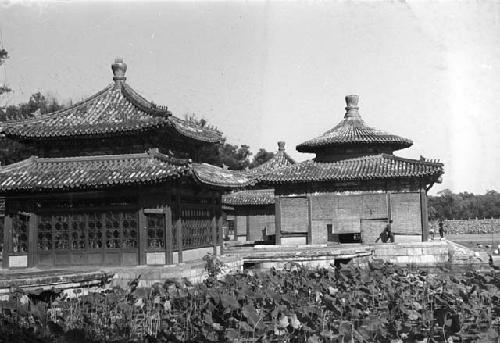 Two people walking on ledges around three ornate buildings