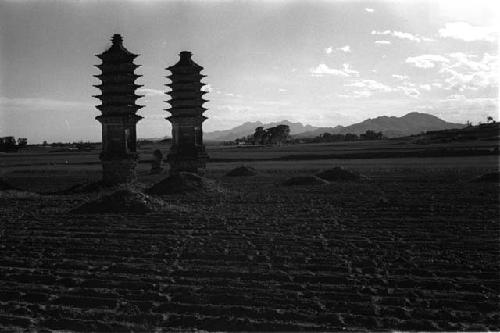 Two tall, narrow pagodas and several mounds in a field