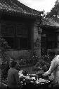 Eleanor Lattimore, a man and a woman seated at table in courtyard