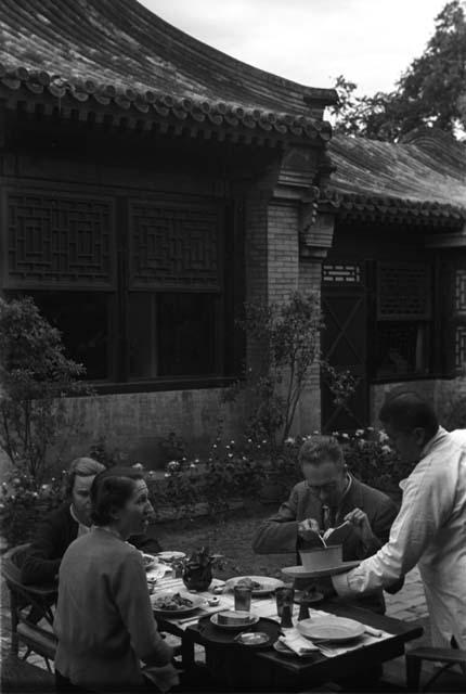 Eleanor Lattimore, a man and a woman seated at table in courtyard