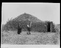 Man and woman in front of earth lodge