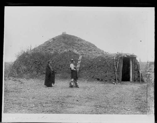 Man and woman in front of earth lodge