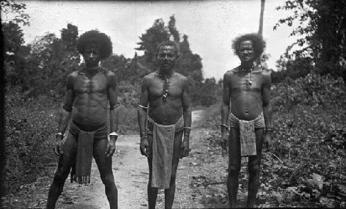 Three men in loin cloths standing on dirt path