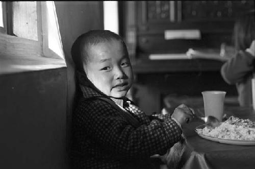 Baby leaning against wall having dinner