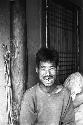 Man smiling wearing a scruffy shirt sitting against wall