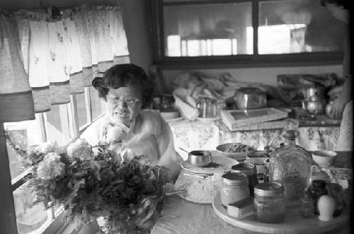 Woman holding flower vase as meal preps in background