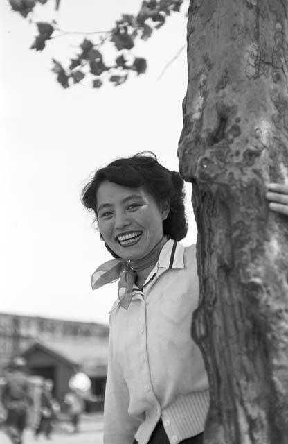 Portrait of woman wearing white top with arm around tree