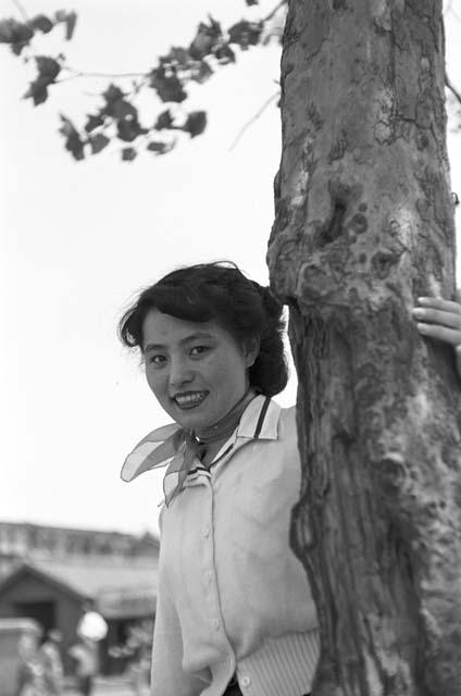 Portrait of woman wearing white top with arm around tree