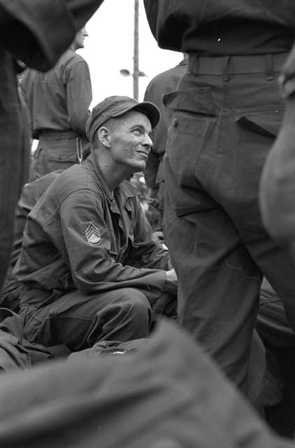 Portrait of soldier in uniform sitting looking up at others around him