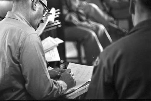 Man sitting in chair writing on paper in lap