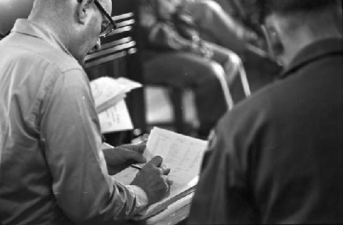 Man sitting in chair writing on paper in lap