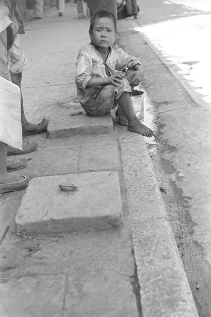 Boy sitting on curb of sidewalk