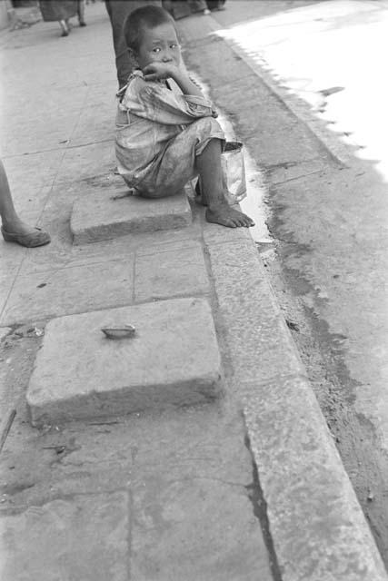 Boy sitting on curb of sidewalk