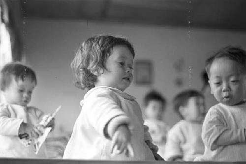 Portrait of baby girl in white garment, babies in background playing