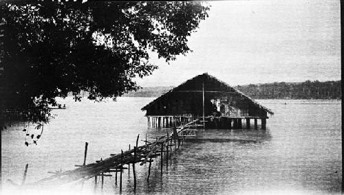 River house on stilts over water with log bridge