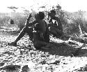 Woman sitting and drinking from an ostrich eggshell, with a child leaning against her, /Gunda sitting behind her