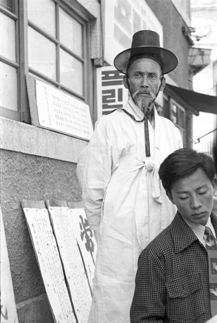 Elderly man standing tall in a white gown over another man