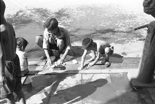 Boys gathering objects at edge of the sidewalk