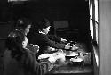 Girl at table reaching over for object by window 2