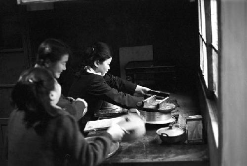 Girl at table reaching over for object by window 2