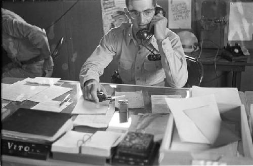 Man sitting at desk on telephone holding a pipe front view