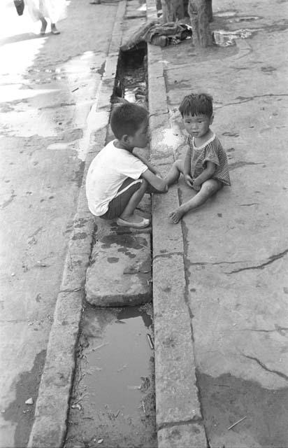 Two boys sitting on the curb of sidewalk