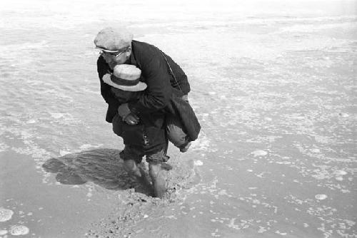 Man carrying Philip Jaffe on his back through shallow water