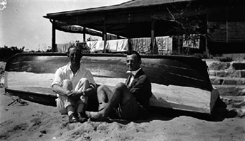 Owen Lattimore and Frank sitting in front of overturned boat