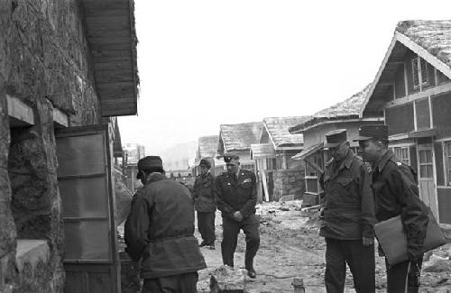 Soldiers standing by oustide of house on dirt road