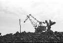 Man carrying brooms, Wrecking ball in background