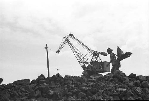 Man carrying brooms, Wrecking ball in background