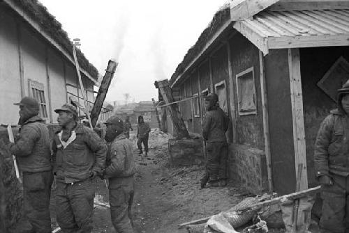 Workers walking along road of ruined houses