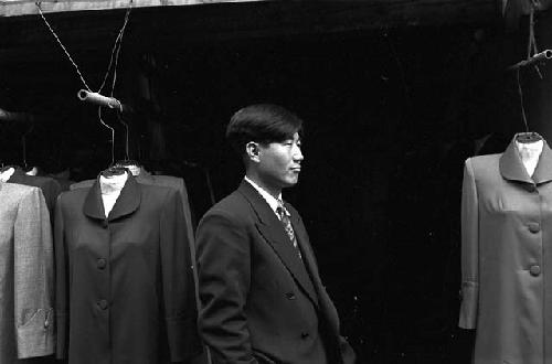 Portrait of man wearing suit standing between racks of suits