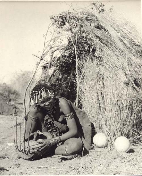 Khuan//a (daughter of !Naishi, headman of Band 5, and //Khuga) sitting in front of a skerm, playing a //guashi